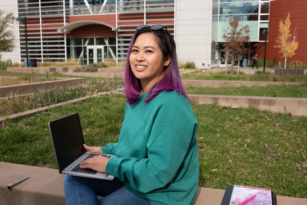 young woman with laptop sitting on wall