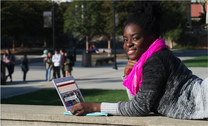 student with pink scarf, lying on stomach with laptop